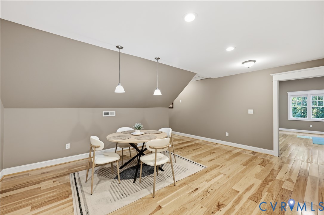 Vaulted ceiling featuring dual pendant light fixtures, wood-finish flooring, and crown molding