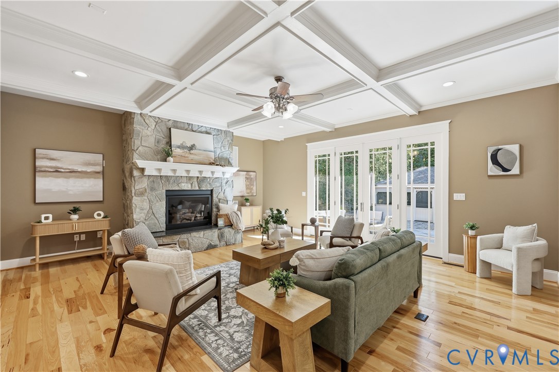 Coffered ceilings, stone-surround fireplace with a wooden mantel, hardwood flooring, and multi-pane glass doors
