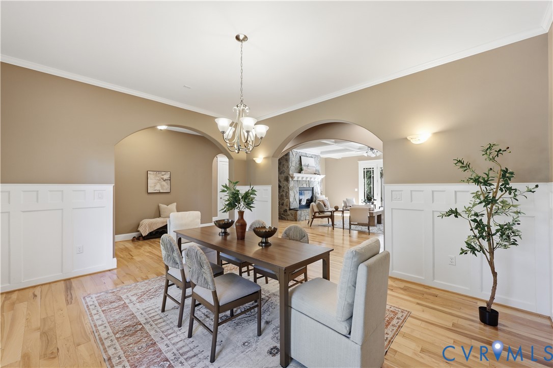 Dining area featuring wood-finish flooring, white wainscoting, arched architectural openings, and a tiered chandelier