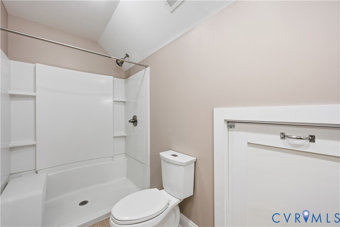 Upstairs Full bathroom featuring a white tub-shower enclosure with integrated shelving, a dual-flush toilet, and white paneled access cabinetry with a polished metal handle