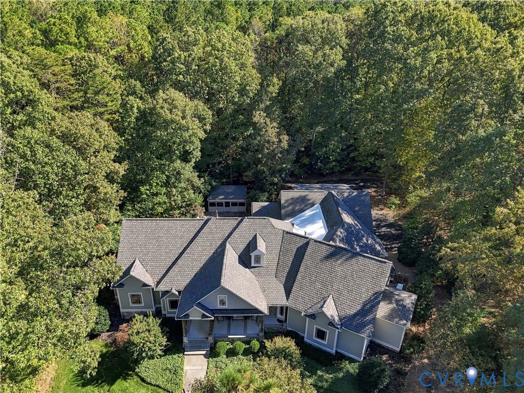 Aerial perspective of a multi-gabled residence featuring shake-style roof shingles, horizontal siding, a covered entryway, and an independent screened structure, all situated on a wooded lot