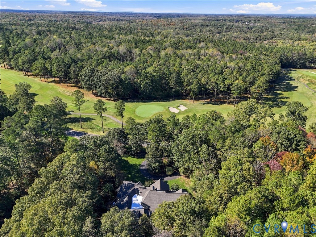 Aerial perspective showcasing a residential property bordered by mature woodlands and a golf course featuring sand bunkers and manicured turf