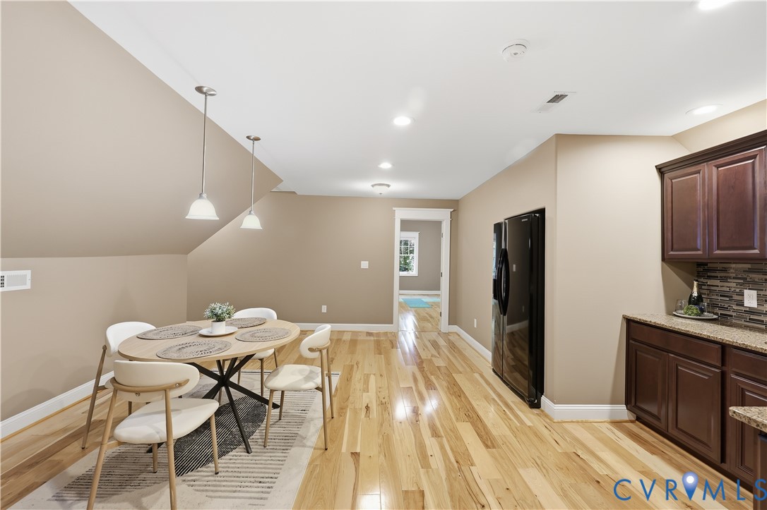 Wood-finish flooring, recessed lighting, dual pendant fixtures, dark-stained cabinetry, and a stacked stone backsplash