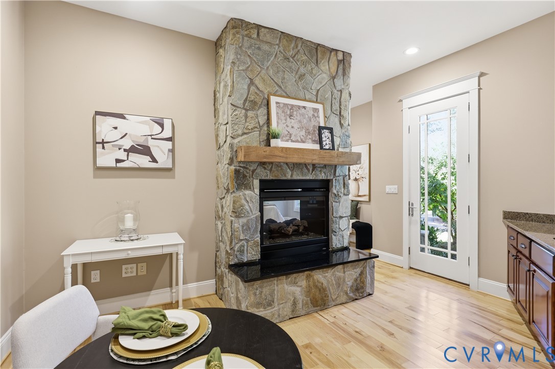 Floor-to-ceiling stone fireplace featuring a dark stone hearth and natural wood mantel, wood-finish flooring, and a glass-paneled exterior door with white trim
