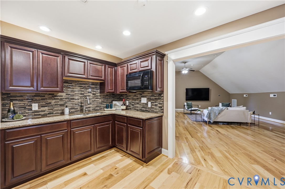Kitchen featuring dark stained cabinetry, stone-finish countertops, tile backsplash, built-in microwave, and wood-finish flooring