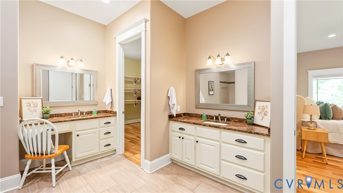 Dual vanity area featuring white cabinetry, stone-finish countertops, framed wall mirrors, and integrated vanity seating