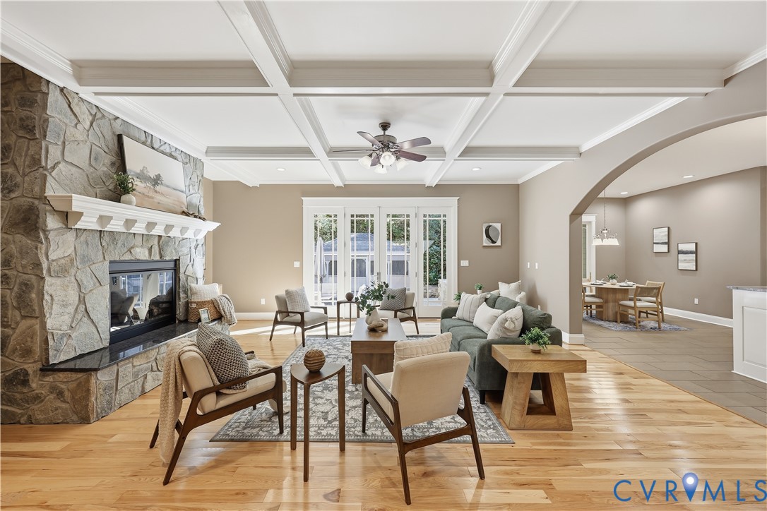 Coffered ceiling, floor-to-ceiling stone-veneer fireplace, wood-finish flooring, glass-paned double doors, and arched entryway