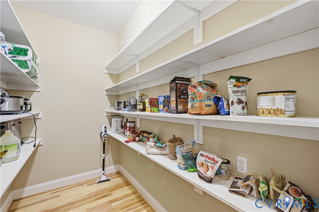 Walk-in storage space featuring multi-level white shelving and wood-finish flooring
