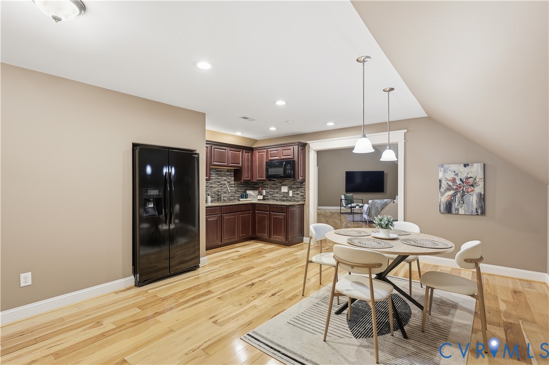 Kitchen featuring dark-finish cabinetry, stone-tiled backsplash, built-in black refrigerator, wood-finish flooring, and dual pendant lighting
