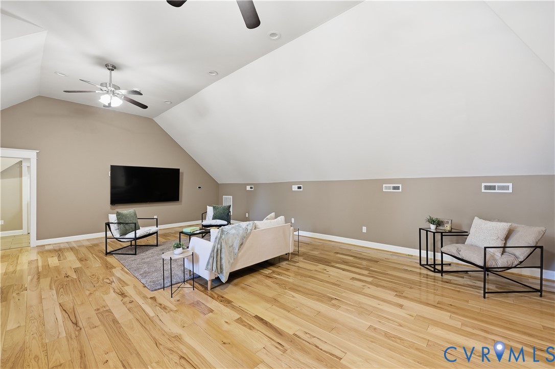 Vaulted ceiling featuring neutral wall tones, wood-finish flooring, and dual ceiling fans