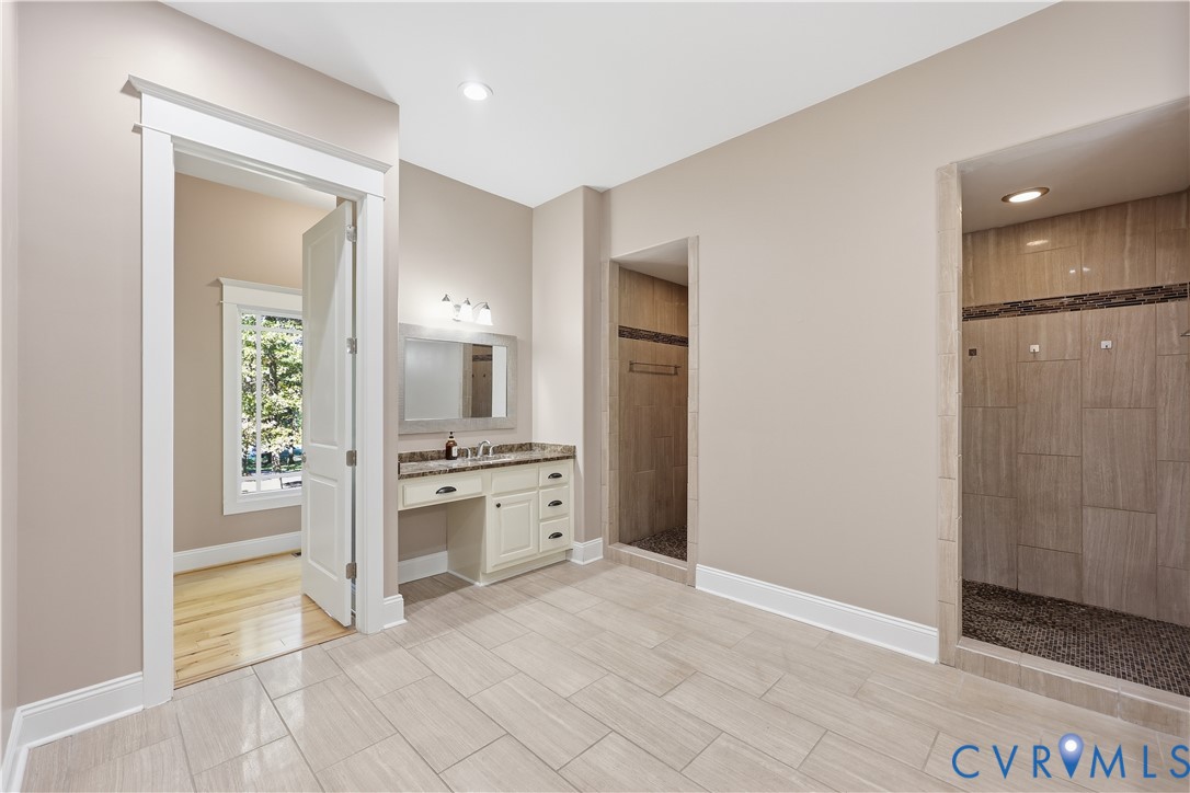 Primary Bathroom 2.  Built-in vanity featuring stone-surfaced countertop, walk-in shower with stone tile surround, pebble-style shower floor, and tile flooring