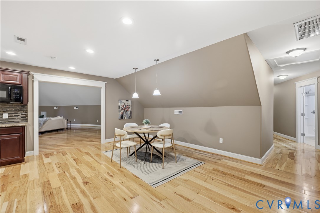 Open floor plan featuring wood-finish flooring, recessed lighting, dual pendant light fixtures, and a vaulted ceiling