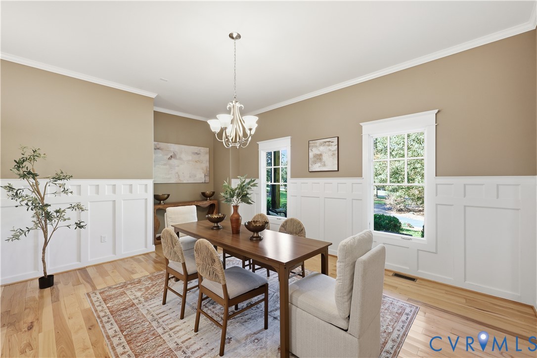 Dining area featuring wood-finish flooring, white wainscoting, crown molding, and a multi-arm chandelier
