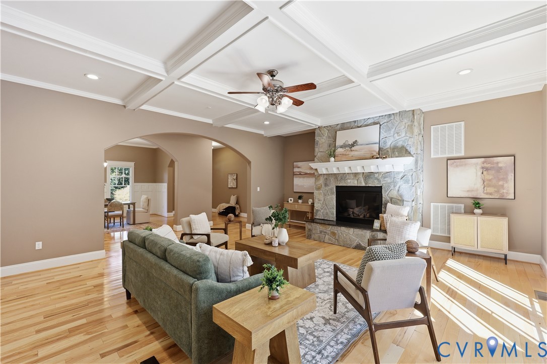 Coffered ceiling featuring recessed lighting, stone-faced fireplace with a mantel, and wood-finish flooring