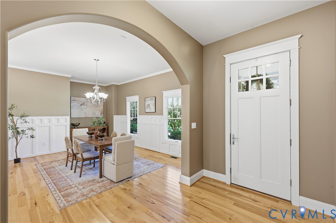 Archway entryway featuring wood-finish flooring, white wainscoting, and a multi-pane glass door with millwork casing