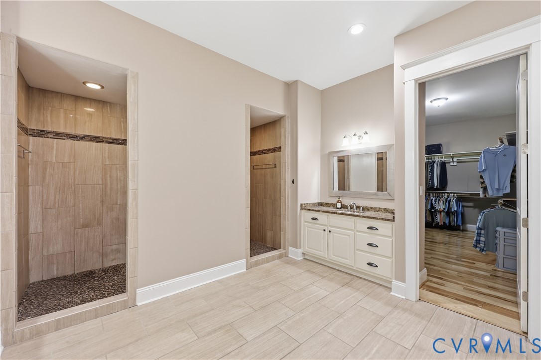 Primary Bathroom 2.  Dual walk-in shower with pebble tile flooring and large-format wall tile, vanity with stone-look countertop, and walk-in closet with wood-finish flooring