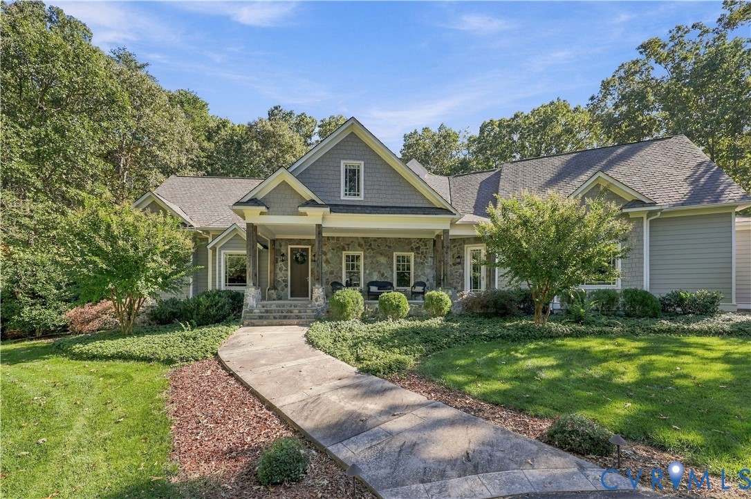 Craftsman-style exterior featuring stone veneer siding, decorative shingle detailing, a covered front porch, and a stamped concrete walkway