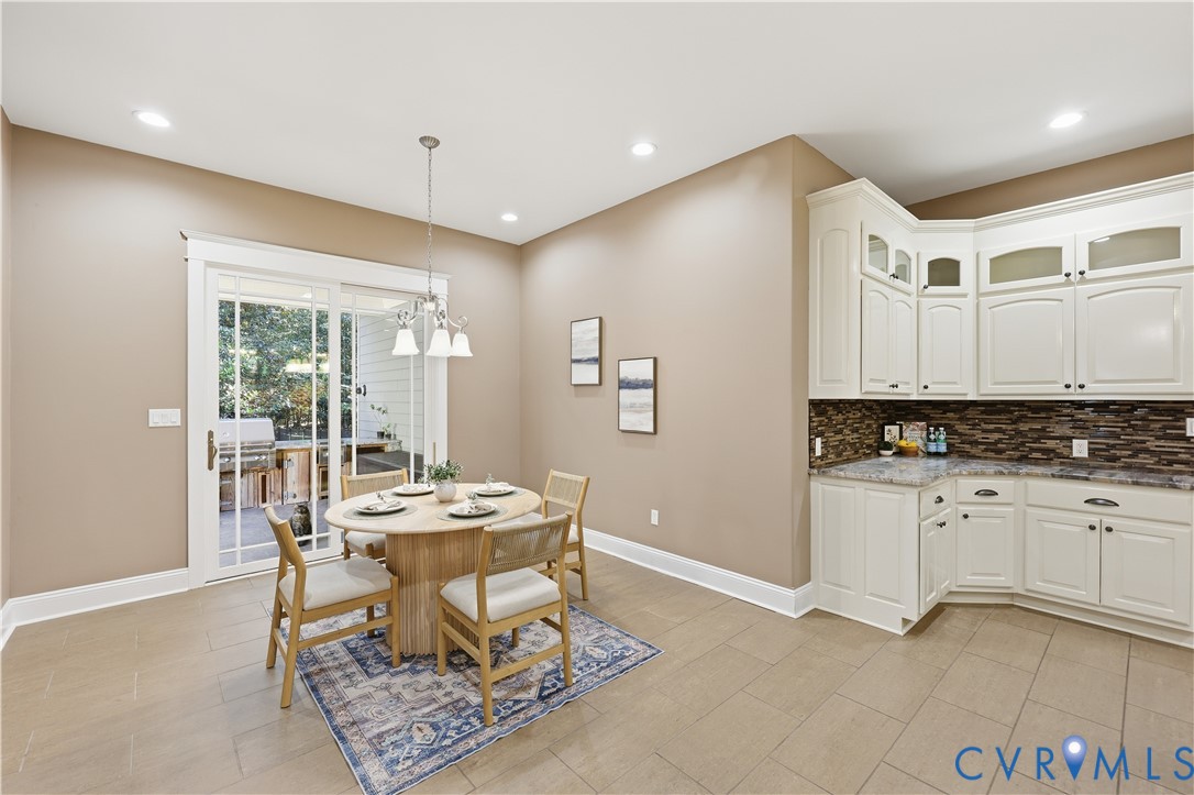 White shaker-style cabinetry, multi-tone stone tile backsplash, stone-finish countertops, tile flooring, and glass-pane sliding doors