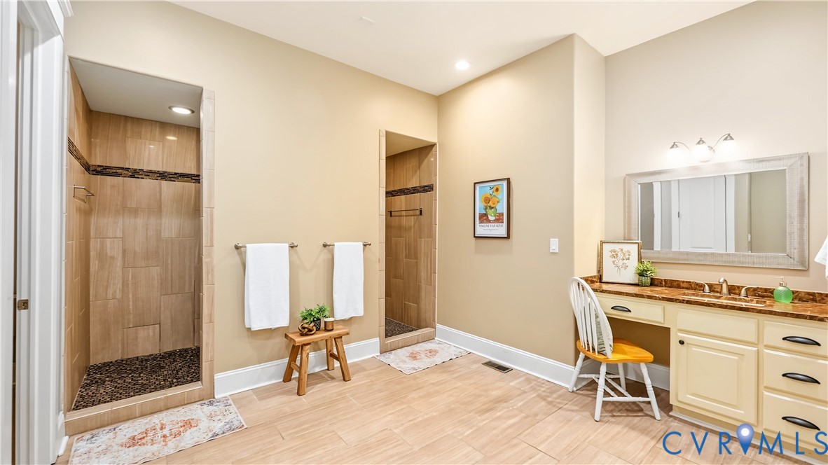 Dual walk-in shower stalls featuring stone-tile surround and pebble-texture flooring, integrated vanity with a stone countertop, and three-light wall-mounted fixture