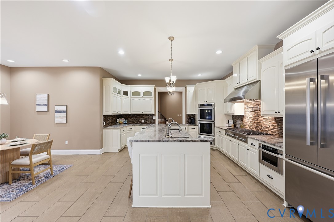 Kitchen featuring white cabinetry, stone-surface island, stainless steel built-in double wall oven, cooktop with a stainless steel range hood, and tile flooring