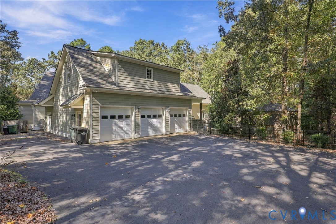 Three-car garage with white paneled doors, light green lap siding, asphalt driveway, and mature surrounding woodland