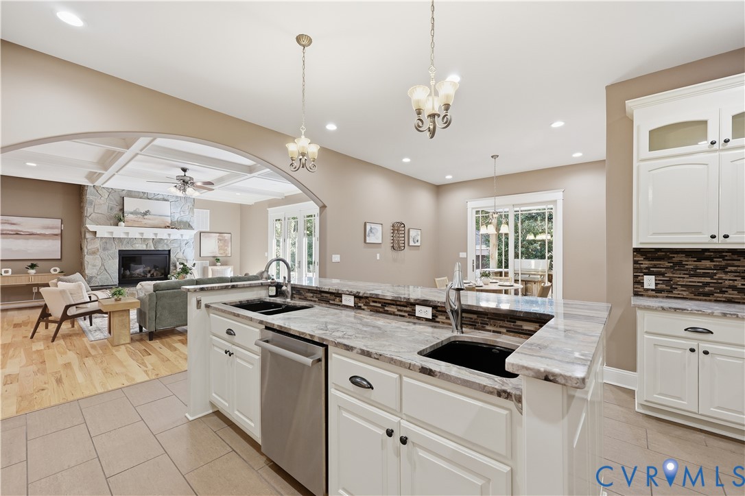 Kitchen featuring stone countertops, white cabinetry, a dual-basin sink with a gooseneck faucet, and recessed lighting, with a coffered ceiling and stone fireplace visible in the background