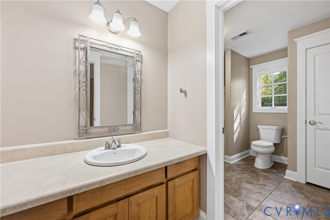 Upstairs Bathroom featuring an oak vanity with a stone-finish countertop, integrated oval sink, decorative metal-framed mirror, and ceramic tile flooring