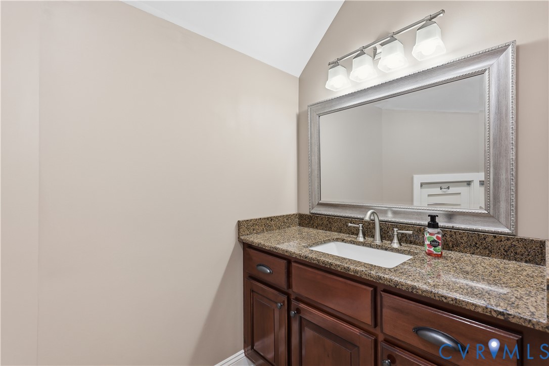 Upstairs Full Bathroom Vanity featuring dark wood cabinetry, a stone countertop with an integrated rectangular sink, a wide-framed wall mirror, and a four-light fixture