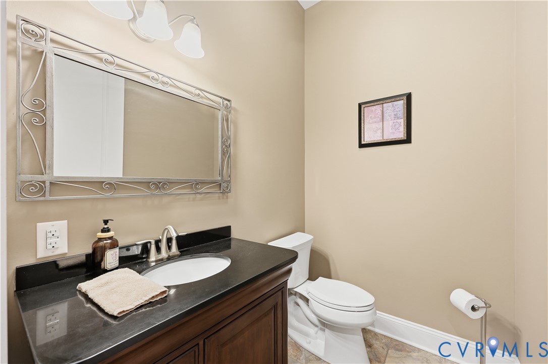 1st Floor Half Bathroom Dark stone-surfaced vanity with an integrated oval basin, decorative metallic-framed wall mirror, three-light overhead fixture, and tile flooring