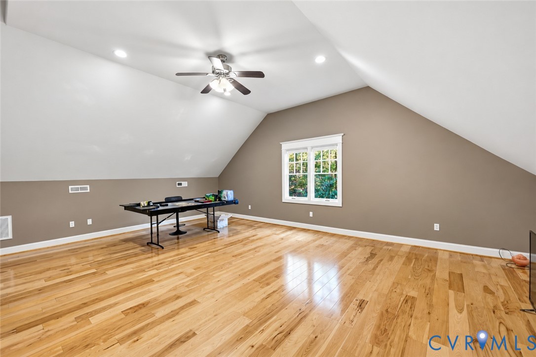 Vaulted ceiling featuring a central multi-blade ceiling fan, recessed lighting, double-hung windows, and wood-finish flooring
