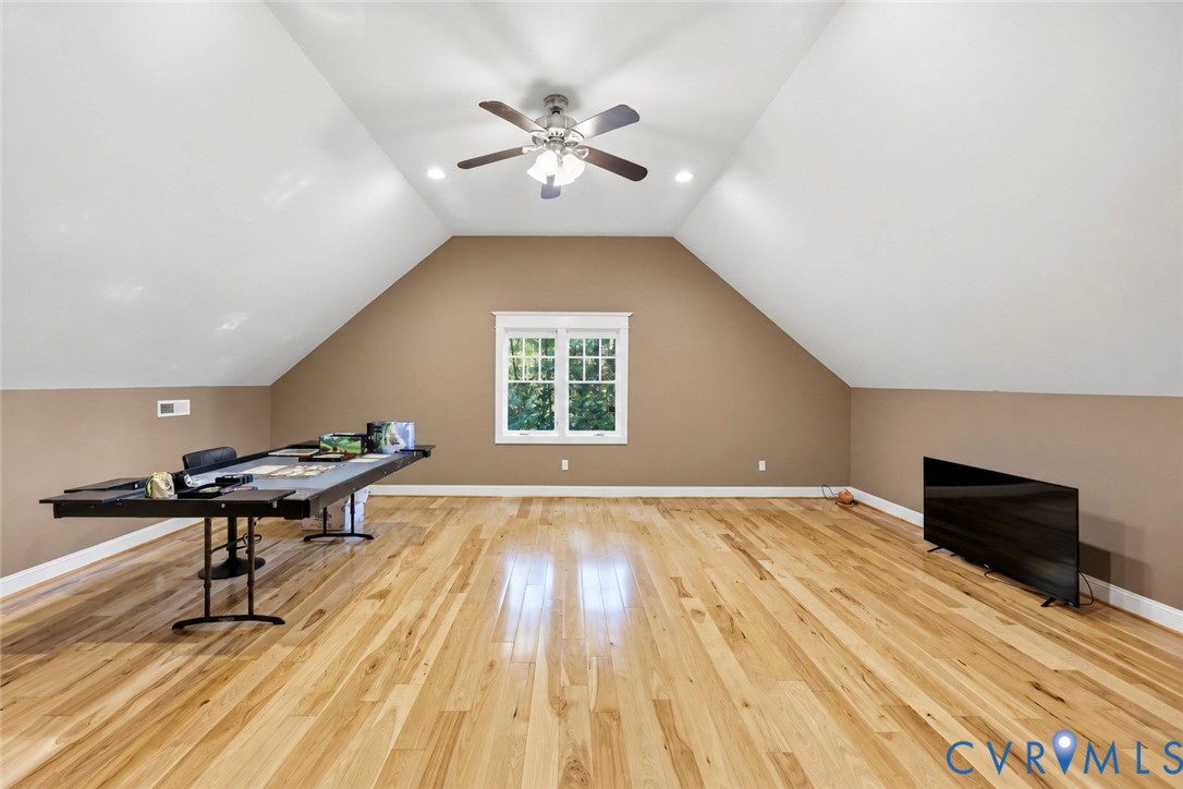 Vaulted ceiling room featuring wood-finish flooring, recessed lighting, a center ceiling fan with integrated light fixture, and a multi-pane window