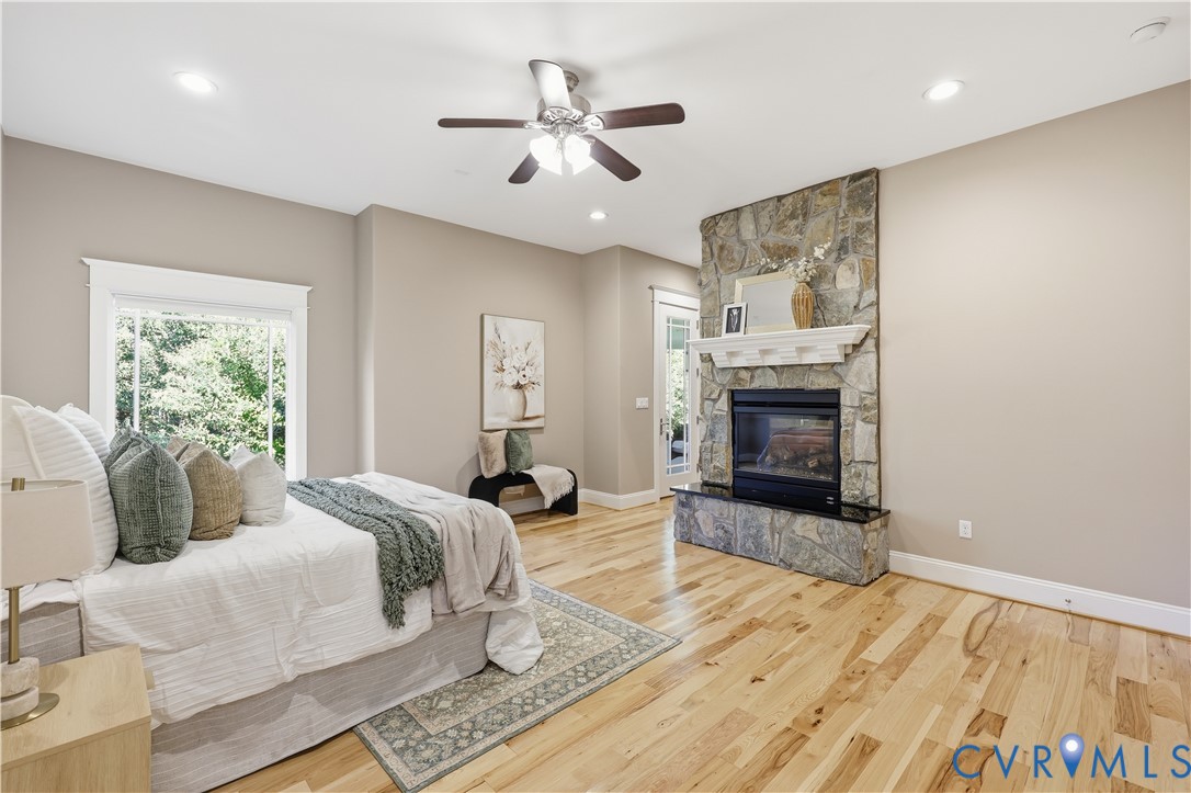 Stone fireplace with a mantle, wood-finish flooring, recessed lighting, ceiling fan, and large-format window