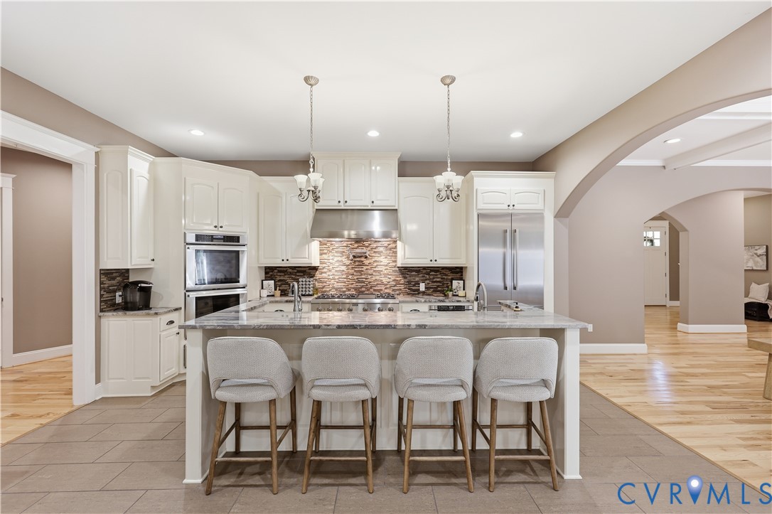 Kitchen featuring white cabinetry, stone-finish countertops, stainless steel appliances, stone tile backsplash, and wood-finish flooring