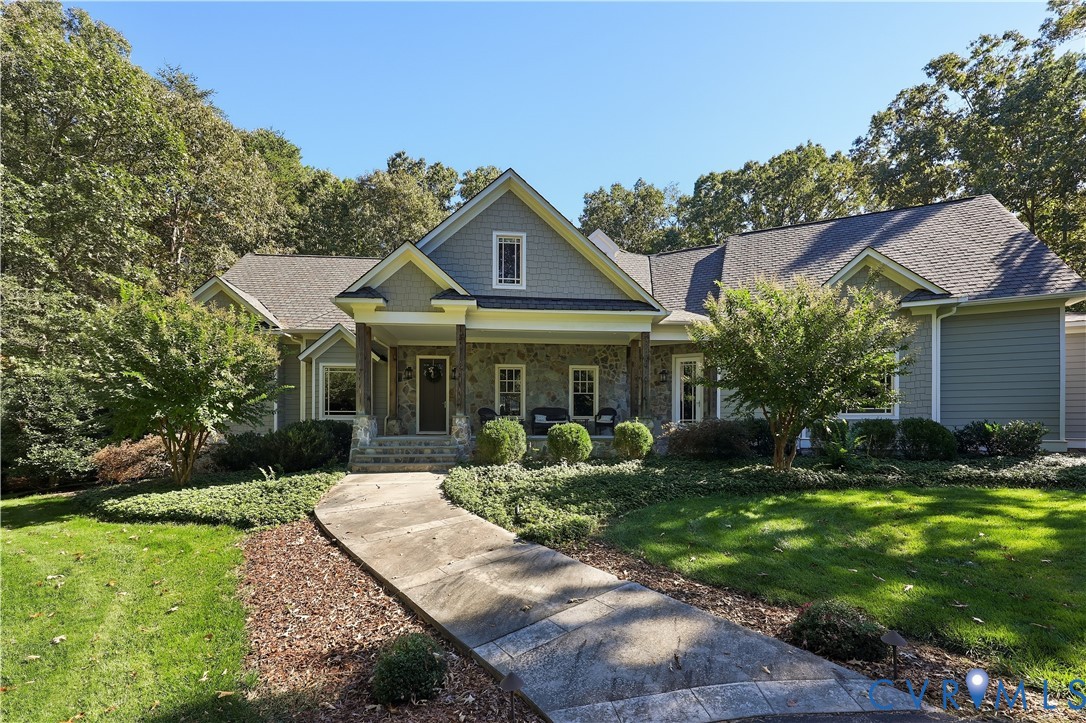 Craftsman-style exterior featuring stone veneer, shingle-pattern siding, covered porch, and a stamped concrete walkway surrounded by mature landscaping