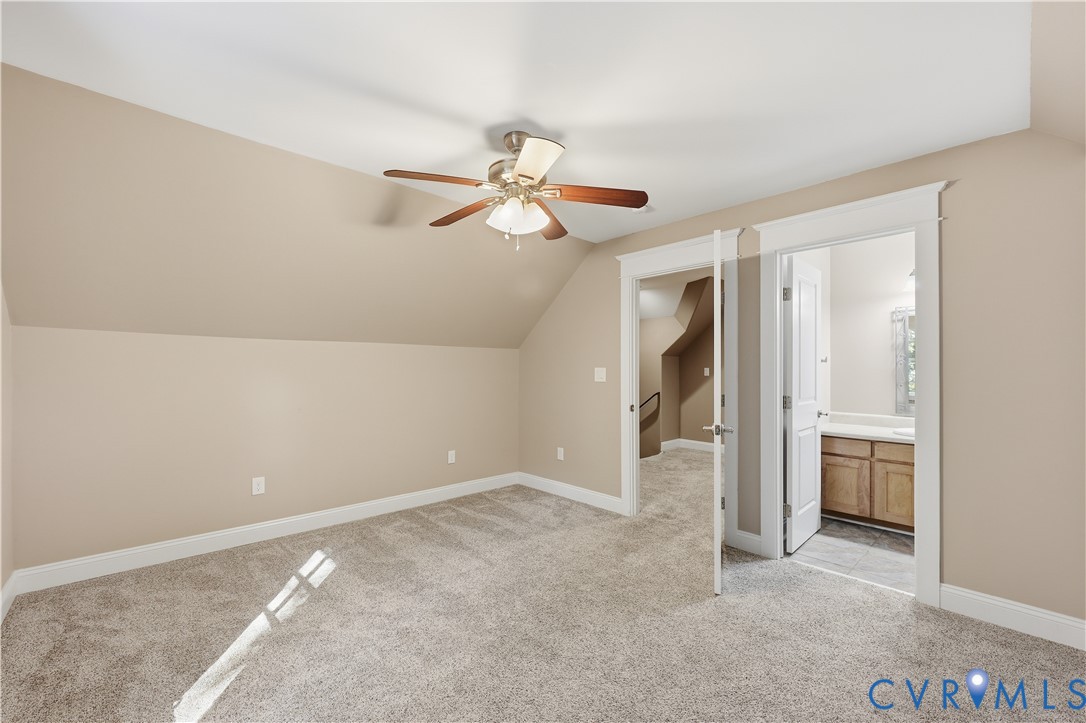 Upstairs Bedroom. Neutral-toned bedroom featuring slanted ceilings, wall-to-wall carpeting, and a multi-blade ceiling fan with a central light fixture