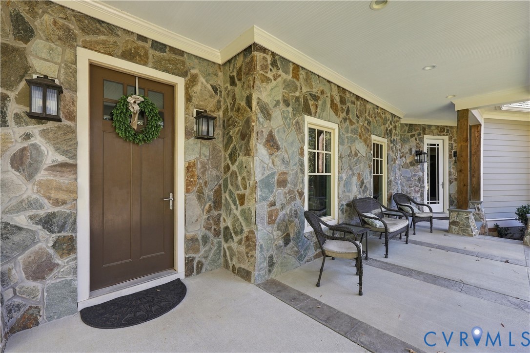 Covered entryway featuring irregular-patterned stone exterior, solid wood entry door, multiple double-hung windows, and recessed lighting