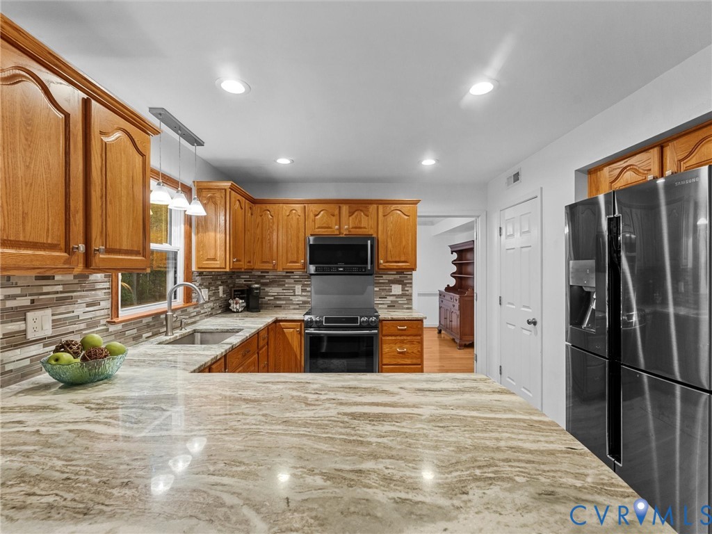 Kitchen featuring wood cabinetry, stone countertops, multi-toned tile backsplash, recessed lighting, and stainless steel appliances