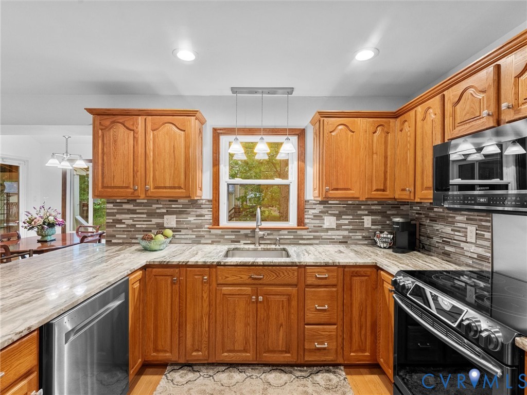 Kitchen featuring natural wood cabinetry, stone-patterned countertops, multi-toned tile backsplash, stainless steel appliances, and recessed lighting