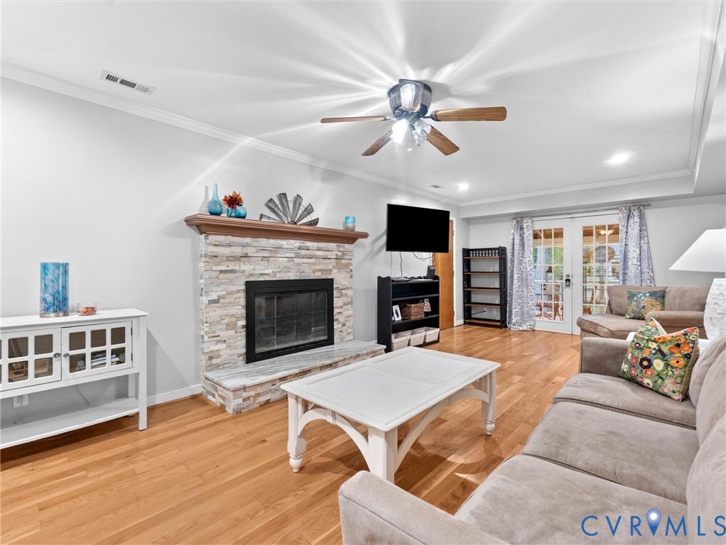 Stacked stone fireplace with a wood mantel, wood-finish flooring, ceiling fan, and French doors