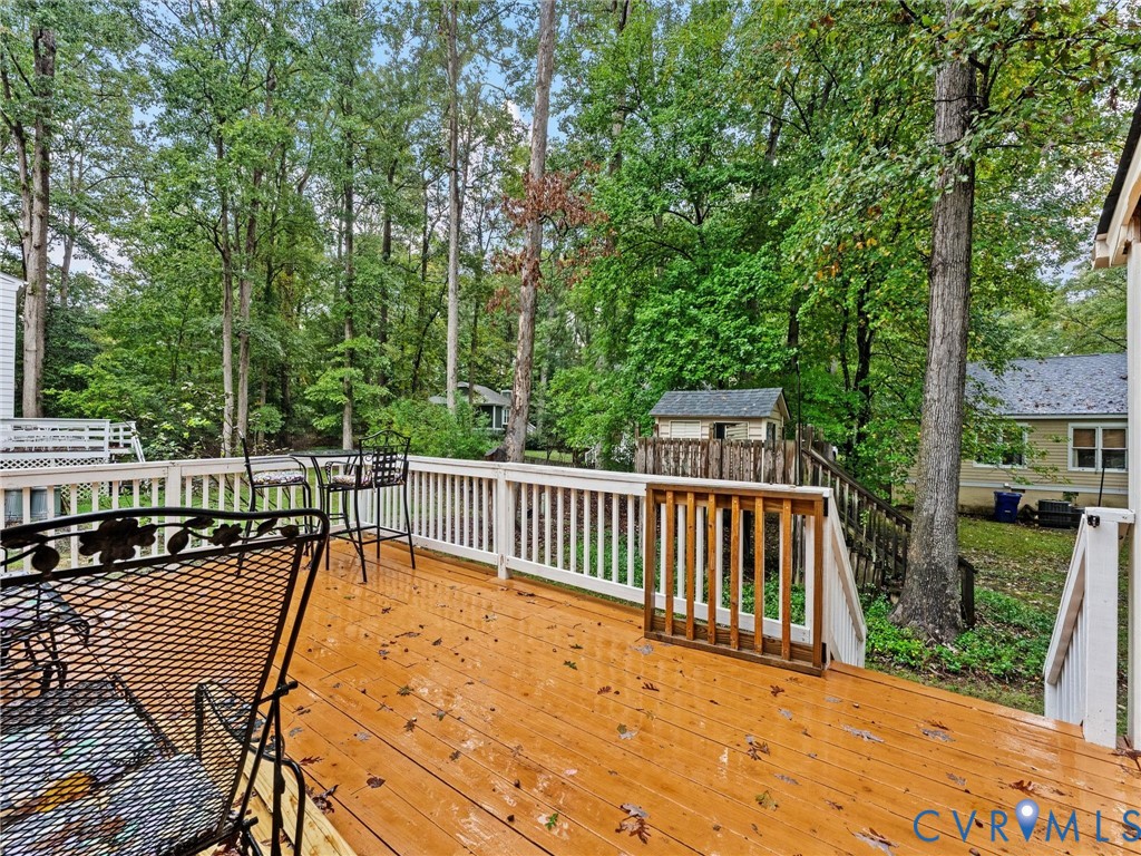 Elevated wood-plank deck featuring white baluster railings and a built-in wooden gate, overlooking a wooded backyard with mature trees