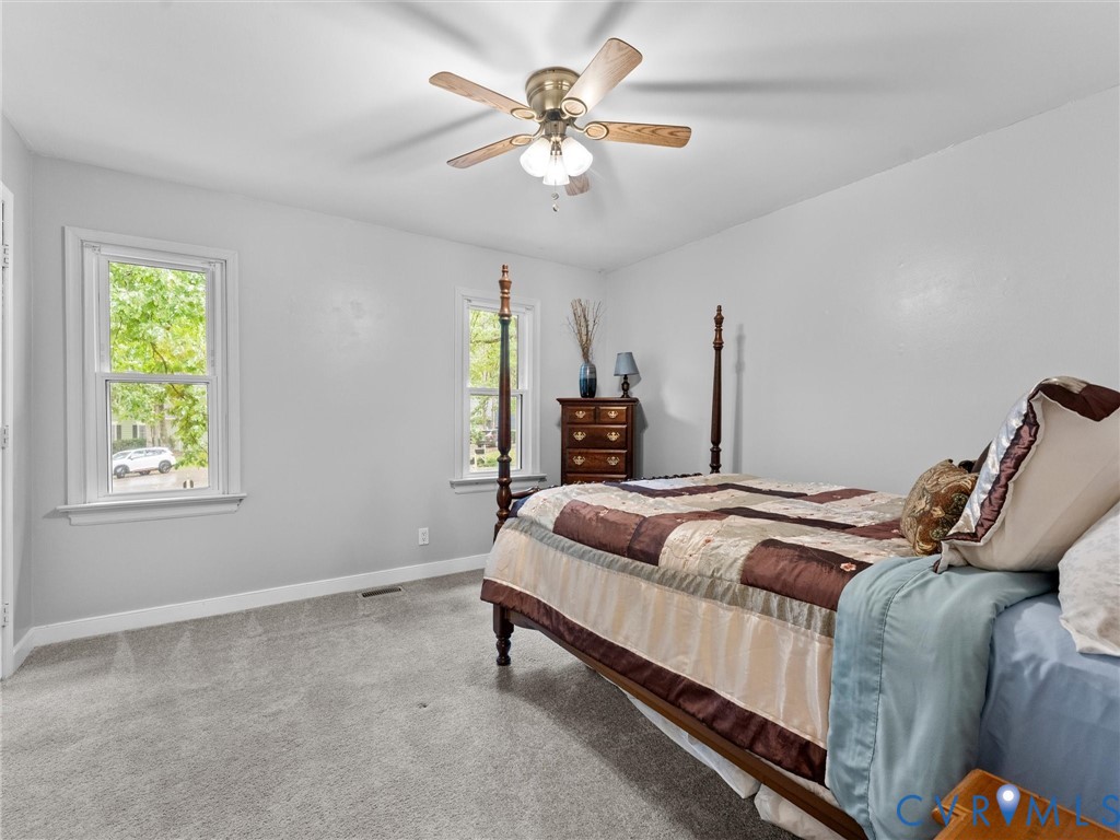 Neutral-toned interior space featuring wall-to-wall carpeting, dual windows with decorative molding, and a central ceiling fan with integrated lighting