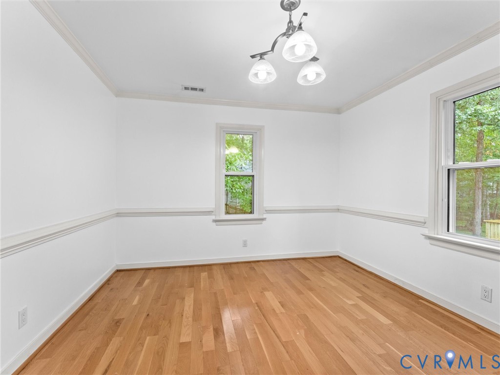 Room interior featuring wood-finish flooring, chair rail molding, crown molding, double-hung windows, and a three-light chandelier