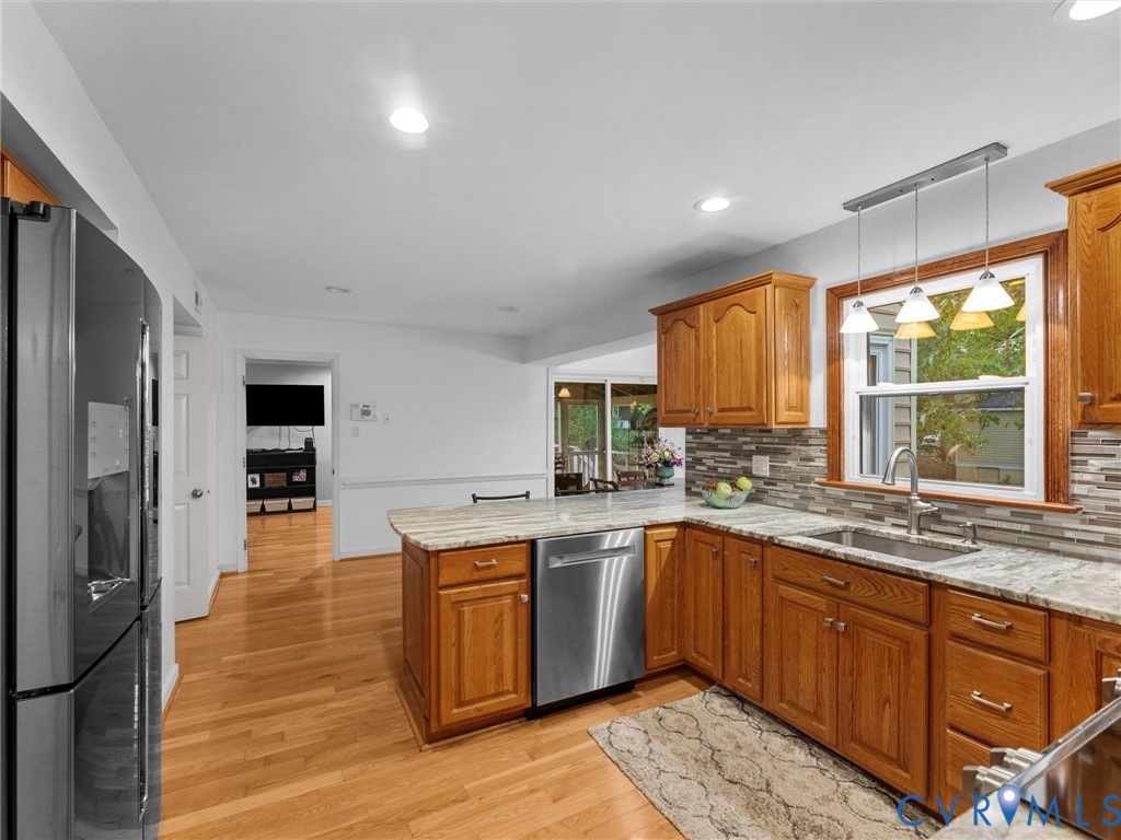 Kitchen featuring wood cabinetry, stone countertops, stainless steel appliances, a multi-tone tile backsplash, and wood-finish flooring