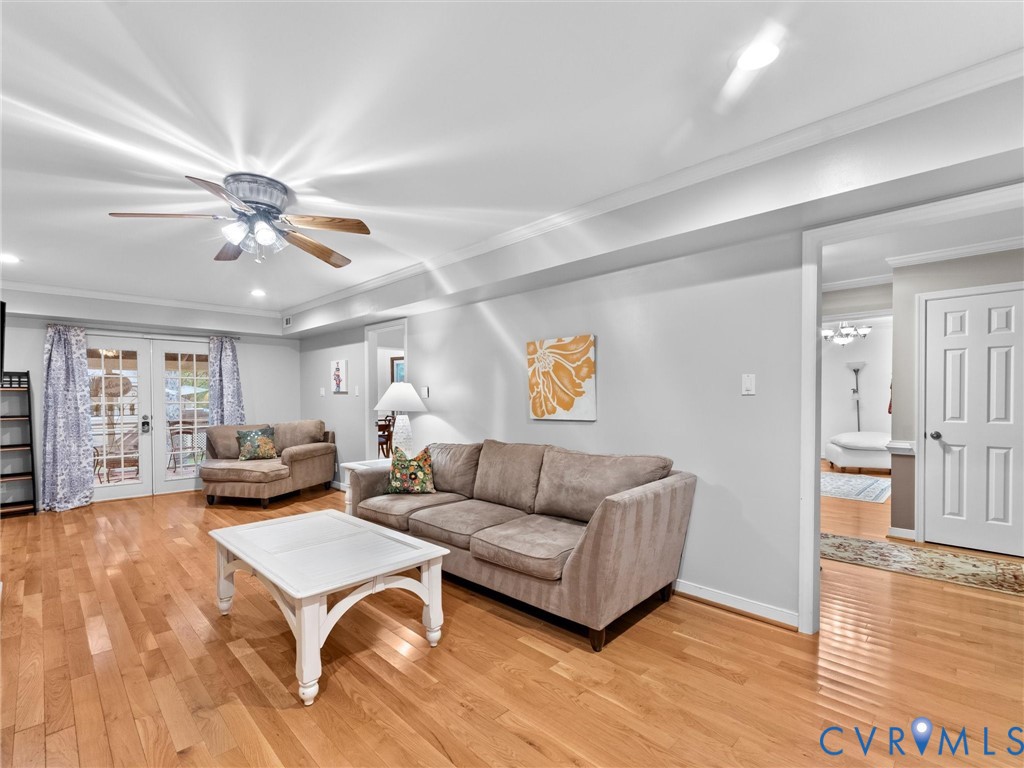 Living area featuring wood-finish flooring, recessed ceiling lighting, a centrally located ceiling fan with integrated lighting, crown molding, and glass-paneled double doors