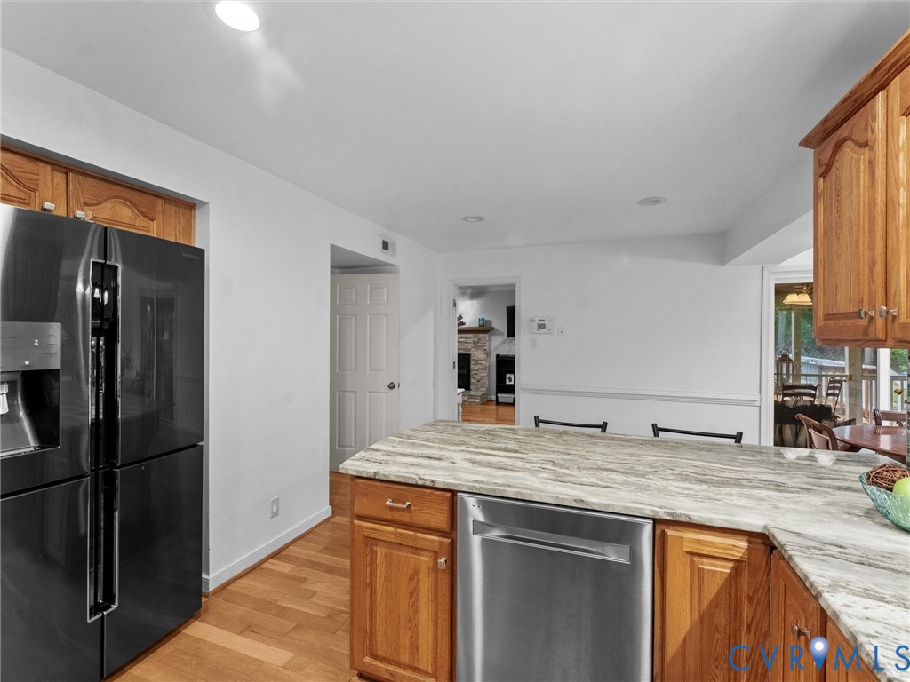 Kitchen featuring wood cabinetry, stone-finish countertops, stainless steel dishwasher, black multi-door refrigerator, and wood-finish flooring