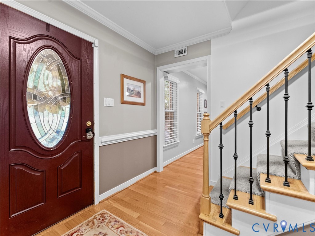 Entryway featuring a dark wood-finish front door with an oval decorative glass insert, wood-finish flooring, and a staircase with a natural wood handrail and iron balusters