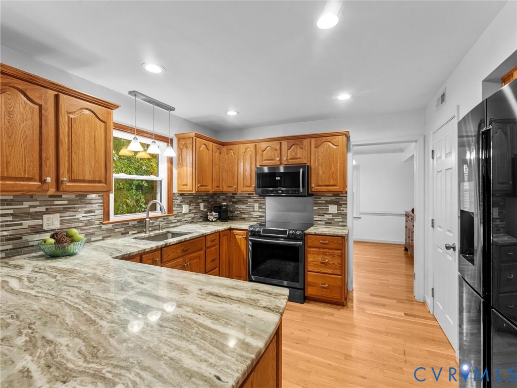 Kitchen featuring wood cabinetry, stone countertops, multi-toned horizontal tile backsplash, stainless steel appliances, and recessed lighting