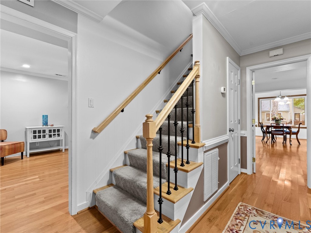 Staircase featuring wood handrails, decorative metal balusters, and carpeted treads, complemented by wood-finish flooring and crown molding