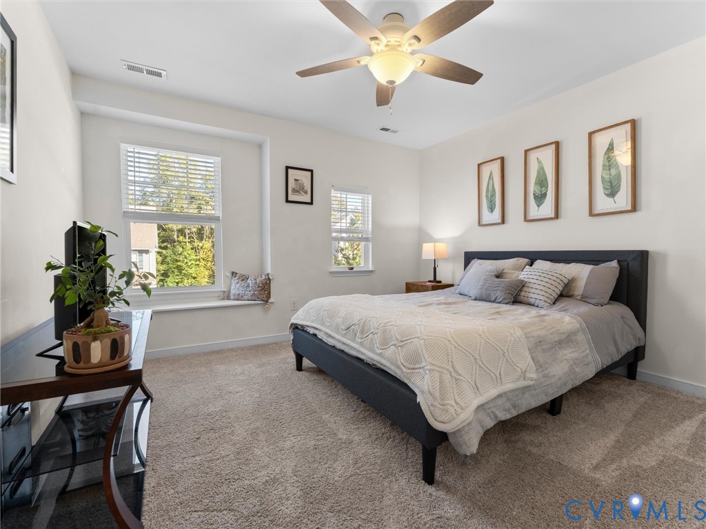 Neutral interior featuring carpeting, double-hung windows, a built-in window seat, and a ceiling-mounted light fixture with a fan