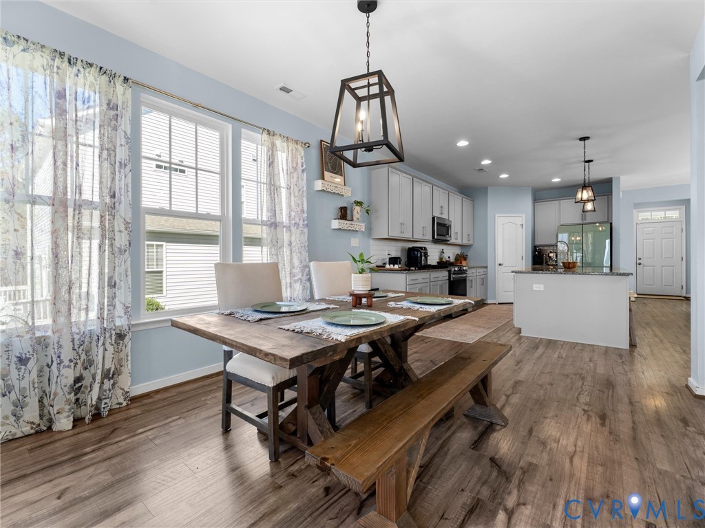Open-concept dining and kitchen area featuring wood-finish flooring, recessed lighting, industrial-style pendant lighting, and light gray cabinetry